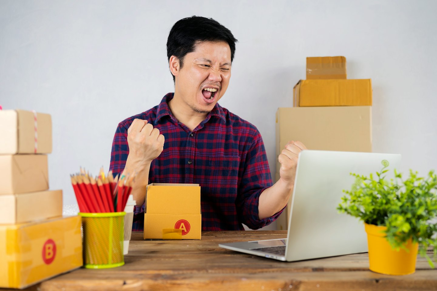 Man celebrates success at his desk surrounded by shipping boxes.